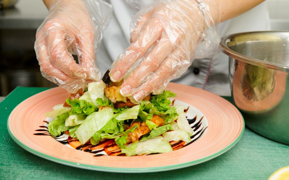 Image showing person wearing gloves, plating a salad. 